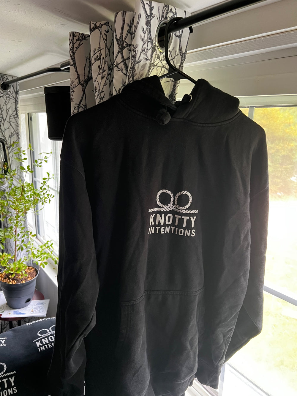Chris’s black KI hoodie hanging beside a window, with the white rope mark on the front.